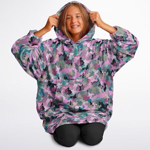May include: A pink, blue, and green camouflage print oversized hoodie with a large pocket on the front. The hoodie has a drawstring hood.