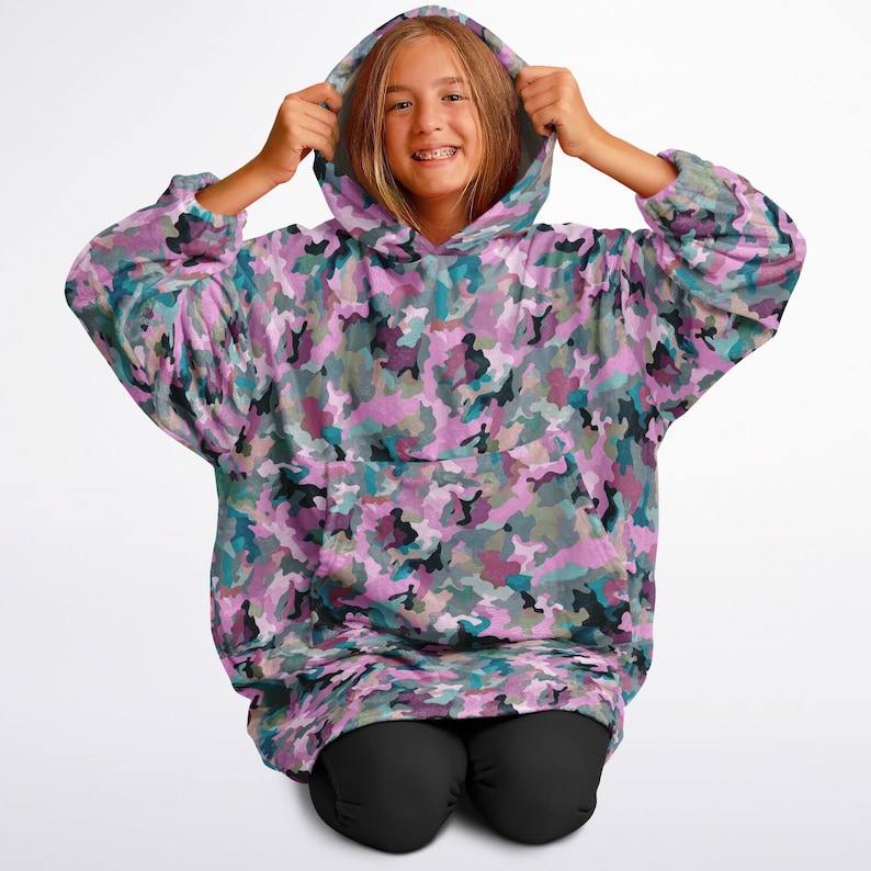 May include: A pink, blue, and green camouflage print oversized hoodie with a large pocket on the front. The hoodie has a drawstring hood.