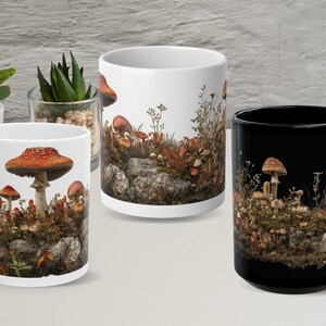 Op de afbeelding: Drie keramische mokken met paddenstoelontwerpen. Eén mok is zwart en twee zijn wit. De mokken bevatten gedetailleerde illustraties van verschillende paddenstoelen, mos en gebladerte. De mokken staan tegen een neutrale achtergrond met potplanten.