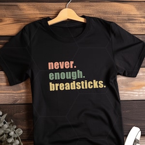 May include: Black t-shirt with the text "never. enough. breadsticks." in colorful retro-style lettering.