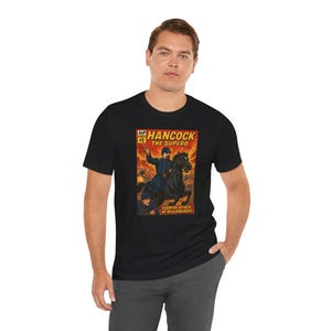 May include: Dark heather grey t-shirt featuring a comic book-style illustration. The graphic depicts a man on a black horse, with the text "Hancock The Superb" and "Counter Attack at Williamsburg".