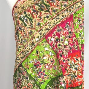 May include: A vibrant textile wrap featuring a patchwork design of green, pink, and orange panels. The fabric is adorned with intricate gold-toned embroidery and numerous small, reflective mirror embellishments throughout the entire surface.