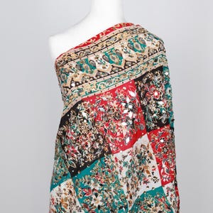 May include: A colorful textile with a patchwork design, draped over a mannequin. The fabric features a mix of red, black, teal, and white squares with floral and geometric patterns. Embellishments include small, reflective accents.