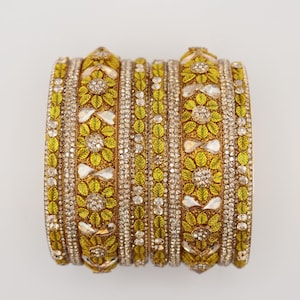 May include: A set of lime green and gold bangles featuring intricate floral patterns and leaf motifs. The bracelets are embellished with clear, sparkling crystals and reflective, teardrop-shaped stones arranged in a repeating, symmetrical design.