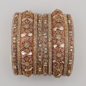 May include: A set of rose gold-toned bangles featuring intricate floral patterns and embedded clear crystals. The collection includes wider bands with embossed leaf and flower motifs interspersed with smaller, thin bands covered in sparkling stones.