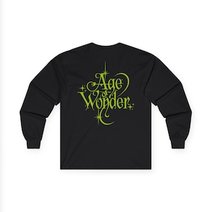 Op de afbeelding: Zwart shirt met lange mouwen met de tekst "Age of Wonder" in een decoratief groen lettertype. De tekst is gecentreerd. Het shirt heeft een ronde hals en lange mouwen.