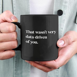 以下が含まれることがあります： 「That wasn't very data-driven of you.」という白い文字が書かれた黒いコーヒーカップ