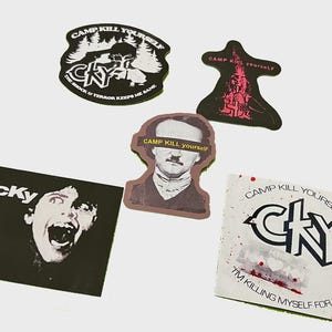 May include: A collection of stickers with various designs and text. One sticker features a screaming face with "cky" text. Other stickers include "CAMP KILL YOURSELF" and "I'M KILLING MYSELF FOR YOU" text. The stickers are in black, white, and red.