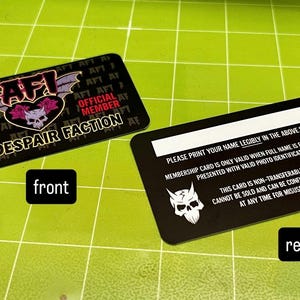 May include: Two black membership cards with rounded corners are displayed on a green surface. The front card features the text "AFI OFFICIAL FAN CLUB THE DESPAIR FACTION" and a skull logo. The rear card has text and a skull logo.