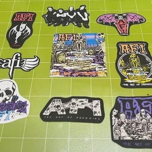 May include: A collection of various stickers with gothic and punk rock themes. Designs include band logos, skulls, bats, and imagery from "The Art of Drowning." The stickers are in black, white, purple, and pink.