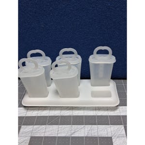 May include: A white plastic popsicle mold set. The set includes five individual molds with handles, each designed to hold frozen treats. The molds sit in a white tray with a rectangular base.