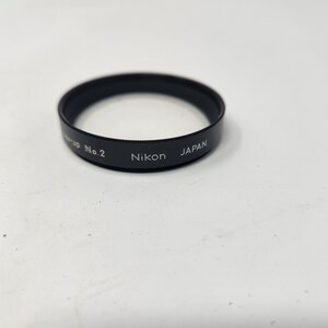 May include: A black camera lens filter with the text "Nikon Japan Group No. 2" printed on the side.