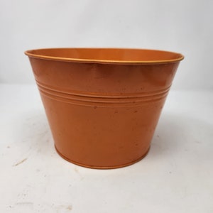 May include: A terracotta colored metal planter pot. The pot is round and has a slightly flared lip.