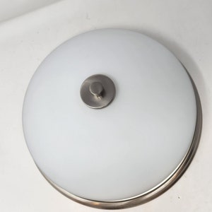 May include: A white ceiling light fixture with a brushed nickel finish and a round, frosted glass shade.