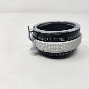 May include: A black and silver Soligor Auto Tele Converter lens with a silver ring and markings that read "Soligor Auto Tele Converter" and "2 2.8 4 5.6 8 11 16".