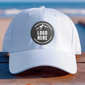 May include: White baseball cap with a black and gray patch that says "LOGO HERE" with a mountain silhouette inside the patch.