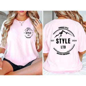 Könnte beinhalten: Pinkes T-Shirt mit einem schwarzen Kreislogo auf der Vorder- und Rückseite. Das Logo zeigt eine Bergkette, den Text "EST 2024", "STYLE LTD" und "EMBRACE STYLE" über der Bergkette und "UNLEASH CONFIDENCE" unter der Bergkette.