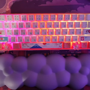 Könnte beinhalten: Eine rosa und weiße mechanische Tastatur mit japanischen Schriftzeichen auf den Tasten. Die Tastatur hat ein Kirschblüten- und Fuji-Design auf der Leertaste. Die Tastatur ist mit rosa und weißen Lichtern beleuchtet.
