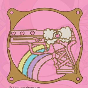 May include: A gold-coloured metal frame with a pink and white gun design inside. The gun has a rainbow design behind it and hearts on the top. The text "kitsune kingdom" is at the bottom of the frame.