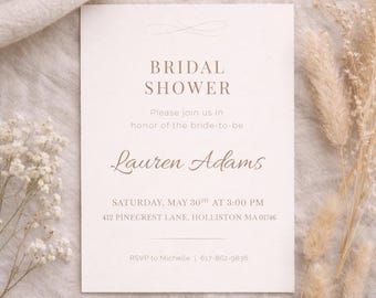 May include: A cream-colored bridal shower invitation with elegant script and the text "Bridal Shower." The invitation includes the name "Lauren Adams" and event details. Dried flowers and greenery are in the background.