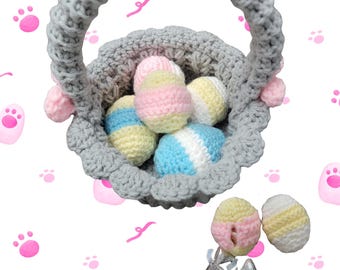May include: A handmade gray crochet Easter basket filled with colorful yarn eggs in pastel shades of pink, yellow, and blue. The basket has a handle and is decorated with pink accents. The basket is surrounded by pink paw prints.