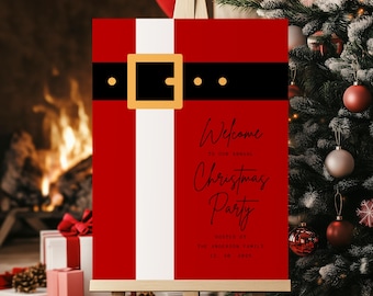 May include: A red Christmas party welcome sign on a wooden easel, designed to resemble Santa's suit. The sign features a black belt with a gold buckle and the words "Welcome to our Christmas Party".