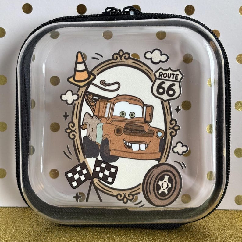 May include: Clear, square zippered case featuring a cartoon image of Mater from the movie Cars, framed by a decorative border. The design includes a Route 66 sign, clouds, and checkered flags. The case has a black trim.