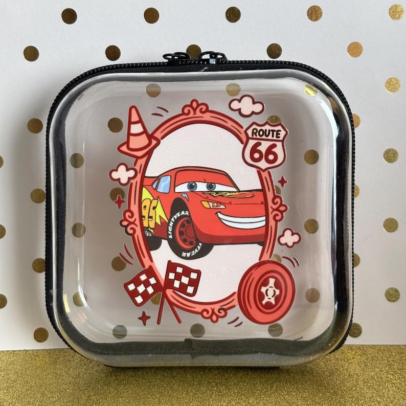 May include: Clear, square zippered case featuring a red cartoon race car with the number 95, a Route 66 sign, and checkered flags. The case has a black trim and a decorative frame around the car.