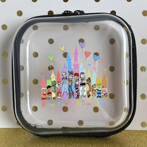 May include: Clear, square cosmetic bag with a black zipper and trim. The bag features a colorful graphic of Disney characters and a castle, with the text "You've Got A Friend In Me". The background has gold polka dots.