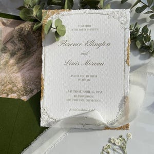 Könnte beinhalten: Eine formelle Hochzeitseinladung mit strukturiertem weißem Papierhintergrund. Die Einladung hat goldene Akzente und eine elegante Schrift, mit den Namen Florence Ellington und Louis Moreau. Datum und Ort sind ebenfalls angegeben.
