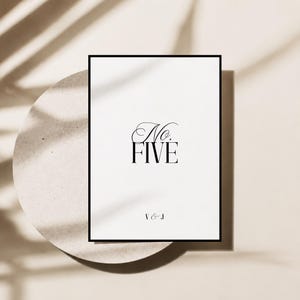 May include: A rectangular white sign with a thin black border featuring the black text No. FIVE in a combination of script and serif fonts, with the initials V & J printed in a smaller serif font at the bottom centre of the white surface.