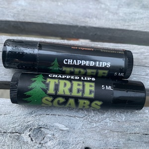 May include: Two black lip balm tubes with green and white labels. The top tube says "Chapped Lips Tree Scab 5 ML" and the bottom tube says "Chapped Lips Tree Scabs 5 ML".