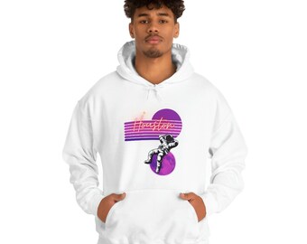 Könnte beinhalten: Weißer Kapuzenpullover mit einem Aufdruck eines Astronauten, der im Weltraum schwebt, mit dem Wort "Houston" in pinkfarbenem Neon-Schriftzug.