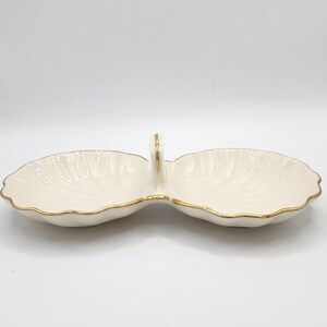 Può includere: Un piatto doppio in porcellana bianca con un bordo dorato e un manico dorato. Il piatto ha la forma di due conchiglie.