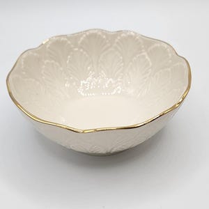 May include: A white ceramic bowl with a gold rim and a scalloped edge. The bowl features a raised floral design.