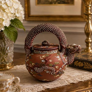 May include: A terracotta teapot featuring a textured dragon-shaped handle and spout, adorned with intricate multi-colored relief patterns of clouds and scales. The lid is circular with a small knob, and the body displays a detailed dragon motif.