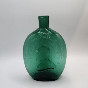 Könnte beinhalten: Eine Vintage-Flasche aus smaragdgrünem Glas mit rundem Körper und kurzem, zylindrischem Hals. Die Flasche trägt den geprägten Text "GEM TAYLOR'S PRENDERS". Die Flasche ist leer und hat eine leichte Textur.