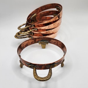 May include: Set of four copper nesting bowls with brass handles. The bowls are stacked on top of each other and have a shiny finish.