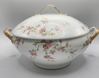 May include: A white porcelain serving bowl with a lid, featuring a delicate floral pattern of pink roses and green leaves. The bowl has gold-coloured handles and trim.