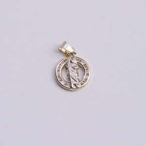 May include: A gold pendant with a religious figure in the center, surrounded by a circle of small clear stones.