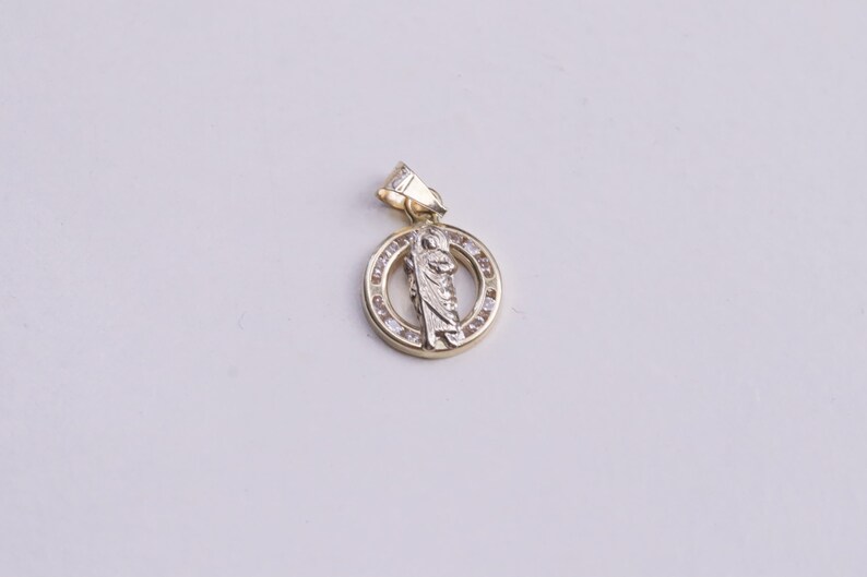 May include: A gold pendant with a religious figure in the center, surrounded by a circle of small clear stones.