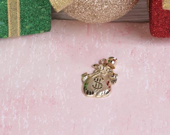 May include: A gold-colored money bag charm with a dollar sign on the front. The charm is on a pink background.