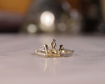 May include: A gold ring with a crown design and small clear stones set in the band.