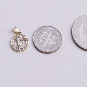 May include: A gold pendant with a small figure of a saint in the center, surrounded by a circle of small clear stones. The pendant is about the size of a US quarter.