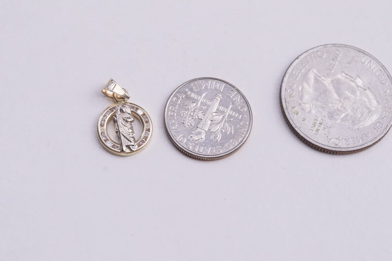 May include: A gold pendant with a small figure of a saint in the center, surrounded by a circle of small clear stones. The pendant is about the size of a US quarter.