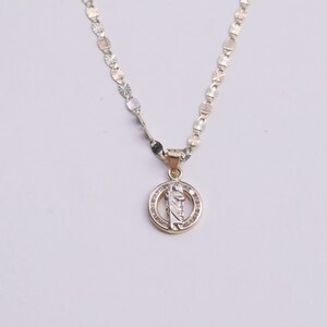 May include: A gold chain necklace with a round pendant featuring a religious figure with a halo. The pendant is decorated with small clear stones.