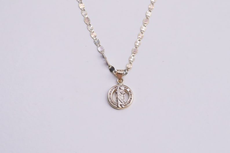 May include: A gold chain necklace with a round pendant featuring a religious figure with a halo. The pendant is decorated with small clear stones.