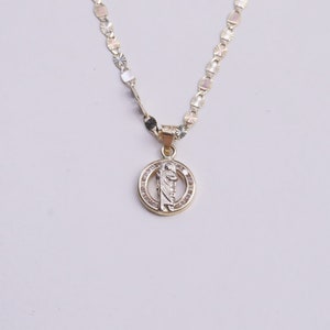 May include: A gold chain necklace with a round pendant featuring a religious figure and small clear stones.
