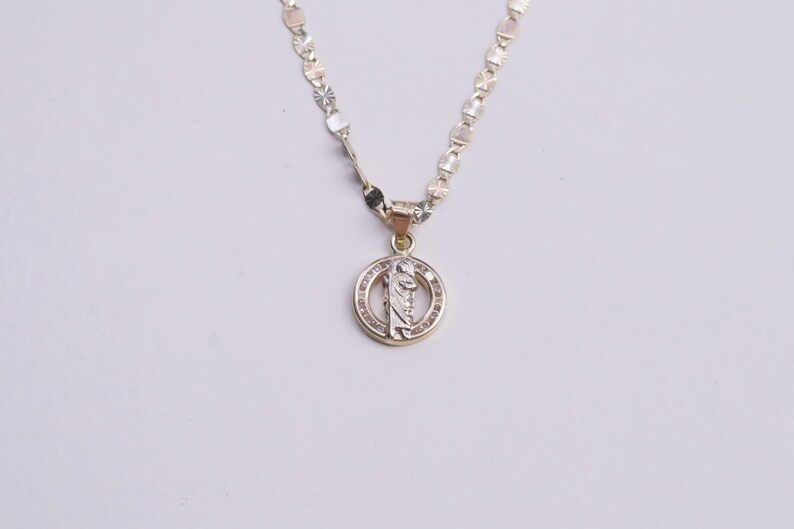 May include: A gold chain necklace with a round pendant featuring a religious figure and small clear stones.