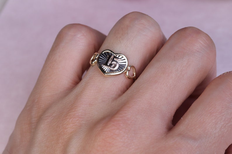 Puede incluir: Un anillo de oro en forma de coraz&oacute;n con el n&uacute;mero "15" grabado en &eacute;l. El anillo tiene un delicado dise&ntilde;o de cadena.